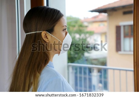 COVID-19 Pandemic Coronavirus Woman home isolation quarantine wearing face mask protective for spreading of virus SARS-CoV-2. Professional nurse looking through the window worried into hospital. Royalty-Free Stock Photo #1671832339