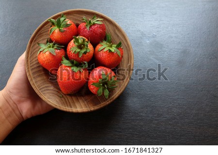 top view hand holding fresh red sweet strawberries on plate wooden on black background