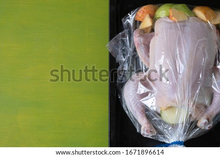 Raw chicken with apples in the plastic oven bag lying on the black baking tray on the green background with a copy space. Healthy way of preparing food