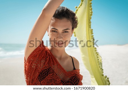Portrait of beautiful latin girl flying green scarf on the beach while looking at camera. Fashion beauty girl with fabric walking on the beach with the breeze that makes her hair fly. Freedom woman.