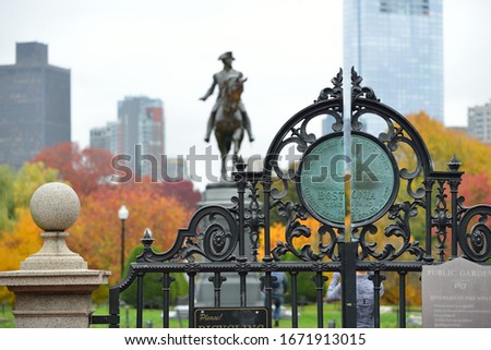 Iron gate and fall colors in Boston Public Garden. George Washington statue and city skyline in background.