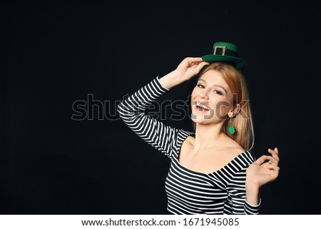 Young woman with green leprechaun hat on black background, space for text. St. Patrick's Day celebration