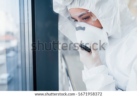 Feels bad and sick. Female doctor scientist in lab coat, defensive eyewear and mask standing indoors.