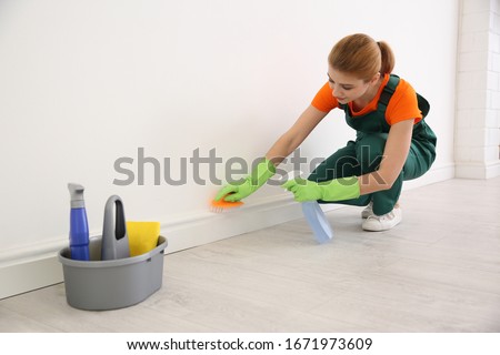 Professional young janitor in uniform cleaning room Royalty-Free Stock Photo #1671973609