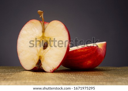 Vibrant bright red apple cut in half with one part laying down and the other standing up in front with seed on a partly out of focus golden surface contrasted against a dark grey studio background