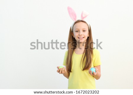 Portrait of a little cute smiling girl with bunny ears and easter eggs in hands on a colored background. Easter background with place to insert text.
