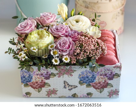 rectangular box with flowers on a white table , close- up with a blurred background, against the background of hat boxes. white Ranunculus, purple rose, white chrysanthemum, freesia, Ozothamnus