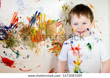 Cheerful happy blue-eyed child in a white T-shirt, painted and stained clothes. The boy looks into the frame, smiles. Royalty-Free Stock Photo #1672083589