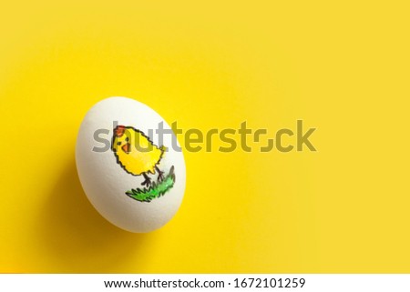One egg with a painted funny chicken on a yellow background. Top view, space for text.