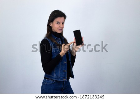 Portrait of pretty middle age woman model holding and showing mobile phone, isolated on gray background studio shot, dark air. Place for your text in copy space.