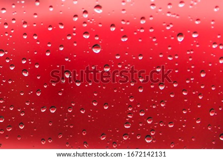 Water droplets from a rain shower on glass with a red background.