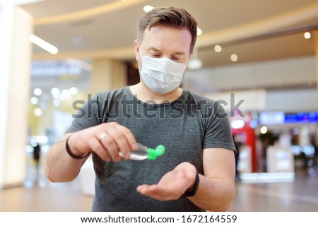 Man wearing disposable medical face mask makes disinfection of hands with sanitizer in airport, supermarket or other public place. Safety during coronavirus outbreak. Epidemic of virus covid. Royalty-Free Stock Photo #1672164559