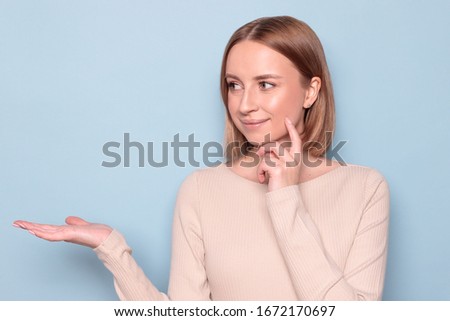 Close up portrait of lovely european woman with short hair present some stuff on palm, holding copy space in the her palm for your advertisement, isolated on blue background. Shopping concept