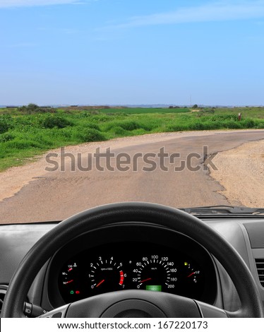 Wheel and dashboard of a car going on the old asphalt road through green fields