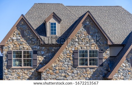 Double gable with dark stone veneer siding,  with triangle shape peaks, on a pitched roof attic at an American single family home neighborhood USA, double sash windows w/ matching dark shutters Royalty-Free Stock Photo #1672213567