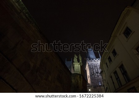 Picture of the lesser town bridge tower of Charles Bridge, also called malostranska mostecka vez in Prague, Czech Republic, at night, surrounded by narrow medieval streets and houses.

