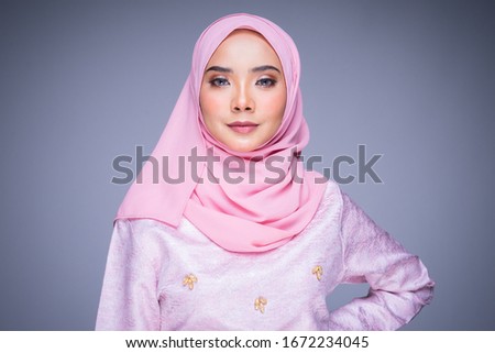 Headshot portrait of a beautiful female model wearing traditional dress and hijab, a lifestyle apparel for Muslim women isolated on grey background. Idul Fitri and hijab fashion concept.