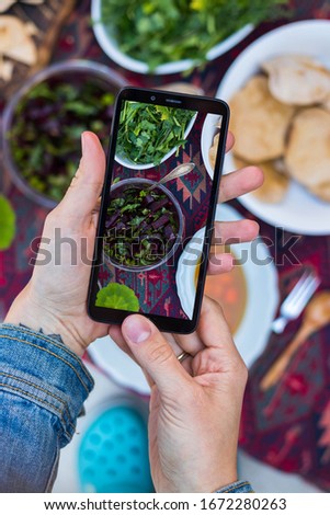 Woman take picture of food with phone at kitchen or summer cafe. Smartphone photography of vegetables dinner or lunch for blogging or social media publications. Vegan vegetarian healthy diet.