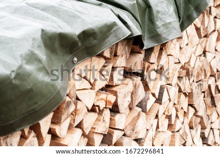 close-up of a stack of chopped firewood covered with a tarpaulin Royalty-Free Stock Photo #1672296841
