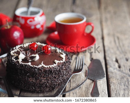Chocolate cake with cherries on a wooden background with red apples and a Cup of tea.Close-up, side view.