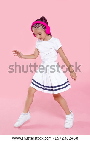 Pretty preschool kid dancing with headphones, over pink background. Happy ittle girl dancing in studio. Full length portrait.