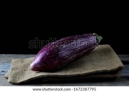 purple striped eggplant laid on jute cloth with rustic wooden backdrop