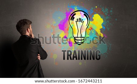 businessman drawing colorful light bulb with TRAINING inscription on textured concrete wall, new business idea concept