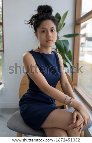 Beautiful Asian woman wearing a blue dress, sitting on a chair.