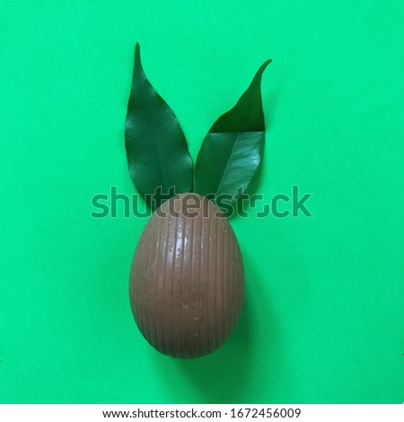 Happy Easter. Minimal Easter concept: chocolate egg and rabbit ears made from fresh leaves on a bright green background