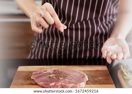 Young female chef prepares fresh beef and sprinkles salt and pepper to fresh beef on wooden block. Concept cooking healthy and cuisine, cooking food, restaurants, hotel business. Bangkok Thailand
