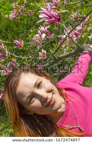 Beautiful girl without makeup in a blooming garden. Woman with long hair without makeup. Natural beauty without makeup. A girl is smiling in a magnolia garden.