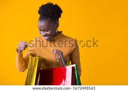 beautiful young african woman on yellow background with credit with packages in hand