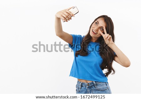 Lifestyle concept. Cheerful brunette female in blue t-shirt, taking selfie on smartphone with kawaii peace sign, tilt head, posting picture herself online, blogging, post for social media
