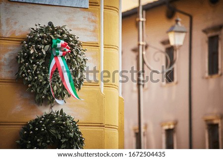 Laurel wreath with Italian flag on the corner of building with blurred street on the behind
