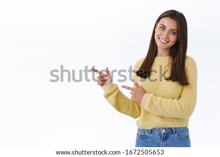 Friendly-looking female student showing you way, pointing fingers up at promo banner, blank white copy space for your ad as give recommendation, suggest visit store, smiling camera pleased