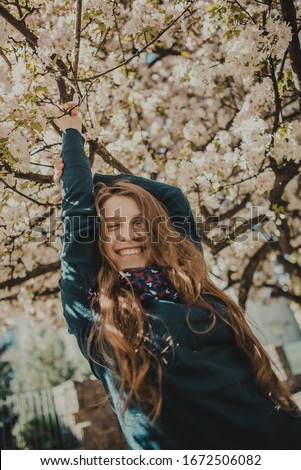 Young blue-eyed blond woman in the park with blooming pink cherry blossoms.
Sakura trees.