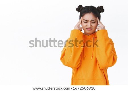 Troubled and uneasy cute asian girl having migraine, feeling headache from studying all day, grimacing feel pain and massaging temples, close eyes trying focus, standing white background