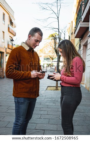 Stock photography of two young people looking at the mobile phone in the street casually and smiling.
