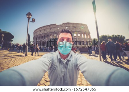 man tourist wearing mask at Colosseum in Rome taking pictures and selfies with smartphone during Coronavirus COVID-19 world outbreak concept. tourist holding a sanitary protective face mask