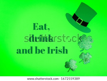 St Patricks Day concept. Shamrocks,  and leprechaun hat on GREEN background. Text EAT, DRINK AND BE IRISH.