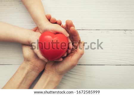 red heart in child and mother hands on white wooden background. concept of love, charity, empathy Royalty-Free Stock Photo #1672585999
