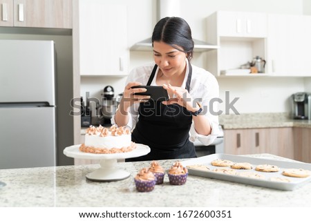 Beautiful female food photographer taking pictures of cake from smartphone for social media in kitchen