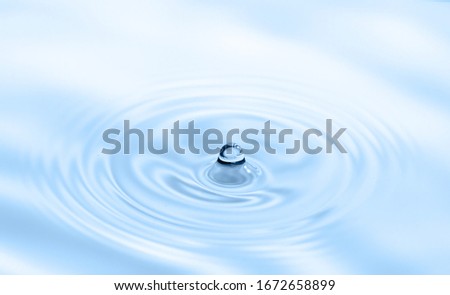 Water drop falling into water making splash and ripples. Light blue nature background.