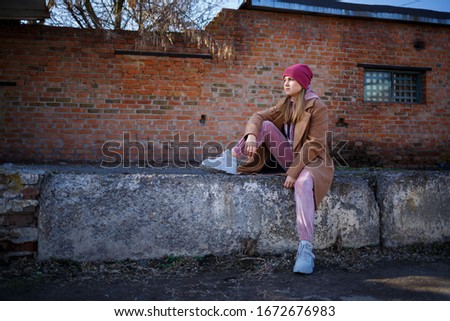 stylish girl model in a brown coat, pink suit and gray boots on the city ruins. The trends of modern fashion. Fashionable image