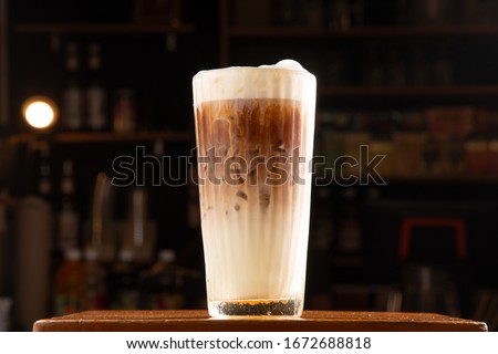 glass of separate layer latte with white foam topping on wood table in blur coffee bar background stock photo