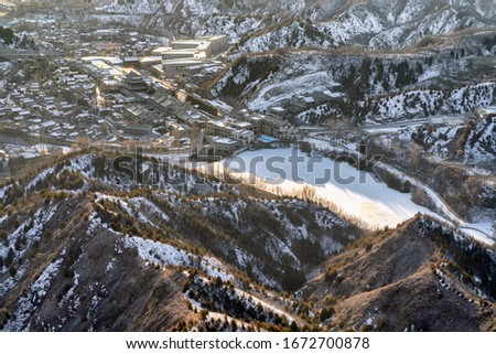 The view on the top of the mountain is covered with snow, below is the city with a frozen lake.