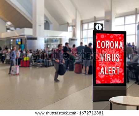 Crowd of people at airport terminal with Corona Virus kiosk or info display