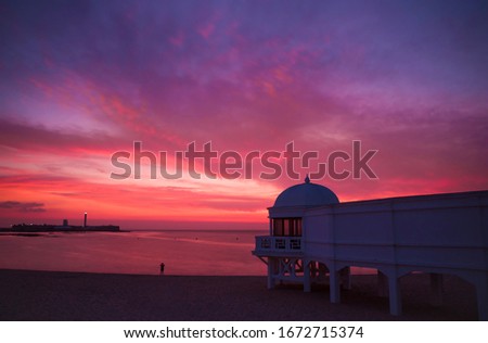 Sunset on the beach with beautiful colors with a bath house and a person taking a picture in Cadiz