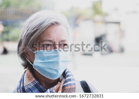 close up of face of mature woman looking away wearing medical mask prevention coronavirus or covid-19 or another type of virus - senior portrait and close up with medicine mask on the face  Royalty-Free Stock Photo #1672732831