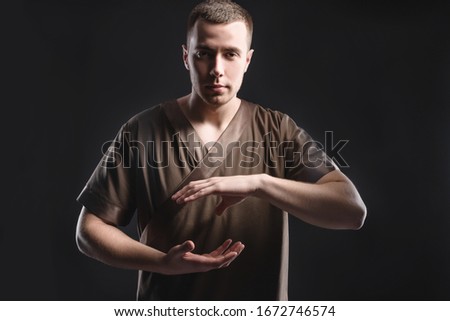 Young professional massage therapist flexes his hands before massage while standing against a dark background